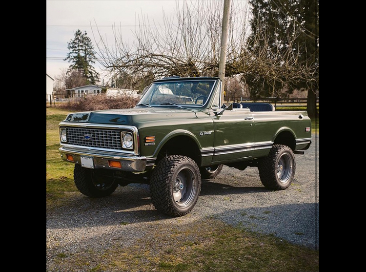 A green truck parked on top of a gravel road.